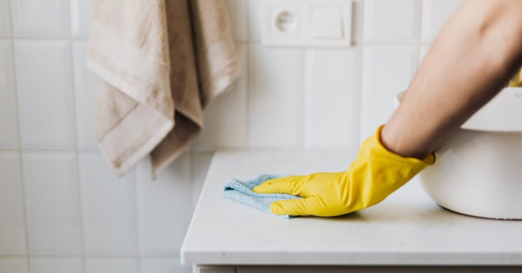 Close-up of a person wearing yellow gloves wiping a bathroom counter with a cloth.